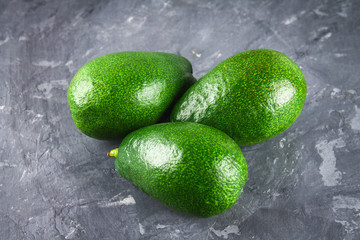 Three greens raw raw ripe avocado fruits on a gray dark concrete table.