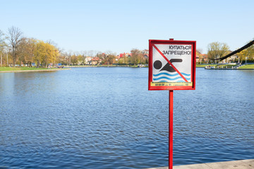 A sign to swim is forbidden on the shore of a lake in a city park in Russia. Text in Russian language.