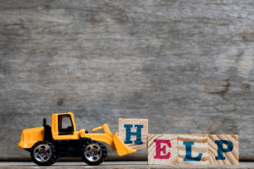 Yellow plastic bulldozer hold letter H to complete word help on wood background