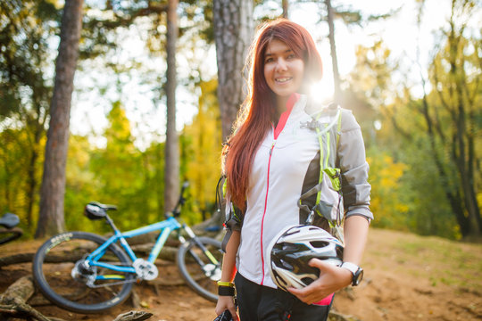 Image of young athletic woman with helmet on background of bicycle at autumn forest