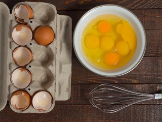 Shells of broken eggs in the container and the egg yolks in the mixer bowl and on a wooden table.