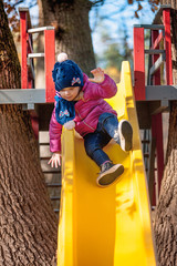 Happy three-year baby girl in jacket on slide