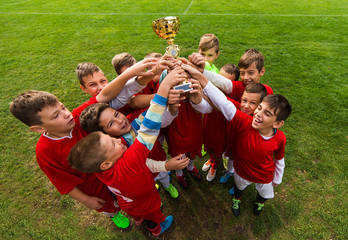 Kids soccer football -  children players celebrating with a trophy after match on soccer field