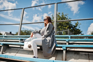 Girl in gray coat with sunglasses at small street stadium.