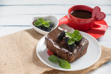 chocolate nut brownie cake decorated with berries and mint leaves. Cup of coffee, sackcloth on white table. selective focus