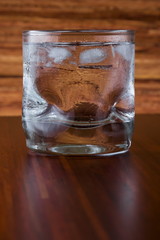 Glass of vodka and ice on wooden background
