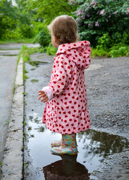The small child in boots and a raincoat runs on pools after a rain.