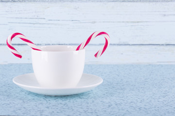 White cup and candy canes against a wooden wall of light-blue color