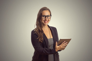 Imagem de mulher linda intelectuel de oculos em pé enquanto segura o comprimido digital em suas mãos e lendo o texto ao fundo cinza. Chefe Mulher de negócios que trabalha no escritório.