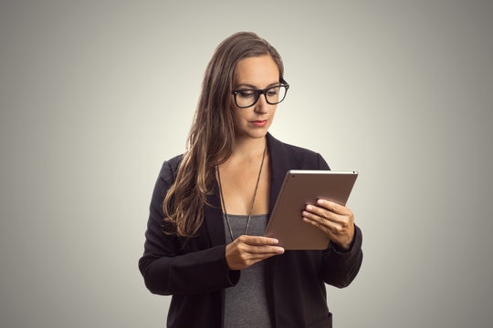 Imagem de mulher linda intelectuel de oculos em p&eacute; enquanto segura o comprimido digital em suas m&atilde;os e lendo o texto ao fundo cinza. Chefe Mulher de neg&oacute;cios que trabalha no escrit&oacute;rio.