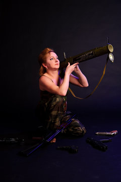 A middle aged, white, woman holds a RPG18 Mukha grenade launcher, with weapon around against black