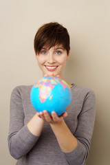 lachende frau zeigt eine weltkugel mit beiden händen
