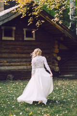 Obraz na płótnie Canvas Blonde bride is walking in fluttering dress on wooden house background. Back view. Artwork