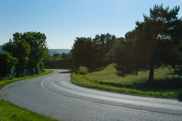 Fototapeta na wymiar Empty asphalt curvy road passing through green fields and forests. Countryside landscape on a bright sunny day in Normandy, France. Transport, industrial agriculture, holiday and road network concept.