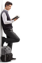 Teen student leaning against a wall and reading a book