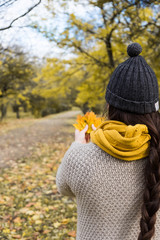 girl in a yellow scarf with maple leaves in her hands in the autumn park
