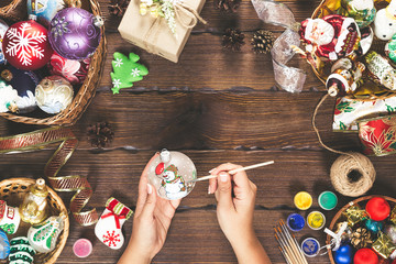 Christmas decorations, balls, toy and gift boxes on old wooden board. Female hands draw New Year...