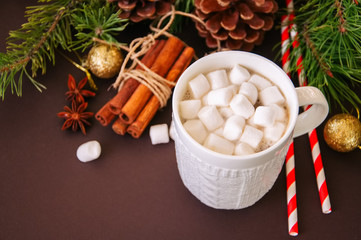 Hot chocolate with marshmallows, fir tree branches, cones, cinnamon and christmas balls on a brown background.