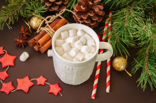 Hot chocolate with marshmallows, fir tree branches, cones, cinnamon and christmas balls on a brown background.
