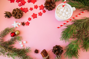 Christmas background with copy space, fir tree branches, hot chocolate with marshmallows, anise, cinnamon, pine cones, red star garland. Pink backdrop.