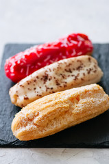 Set of assorted eclairs served on a slate board on a white stone background.