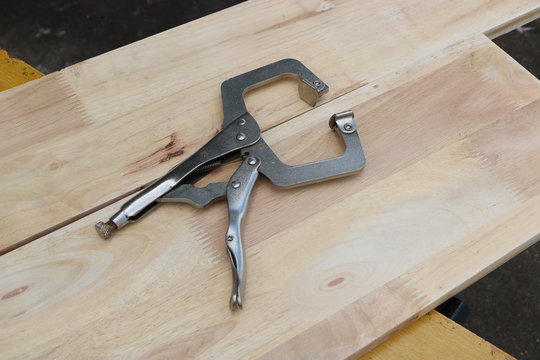Metal vise grip locking clamp on wooden background