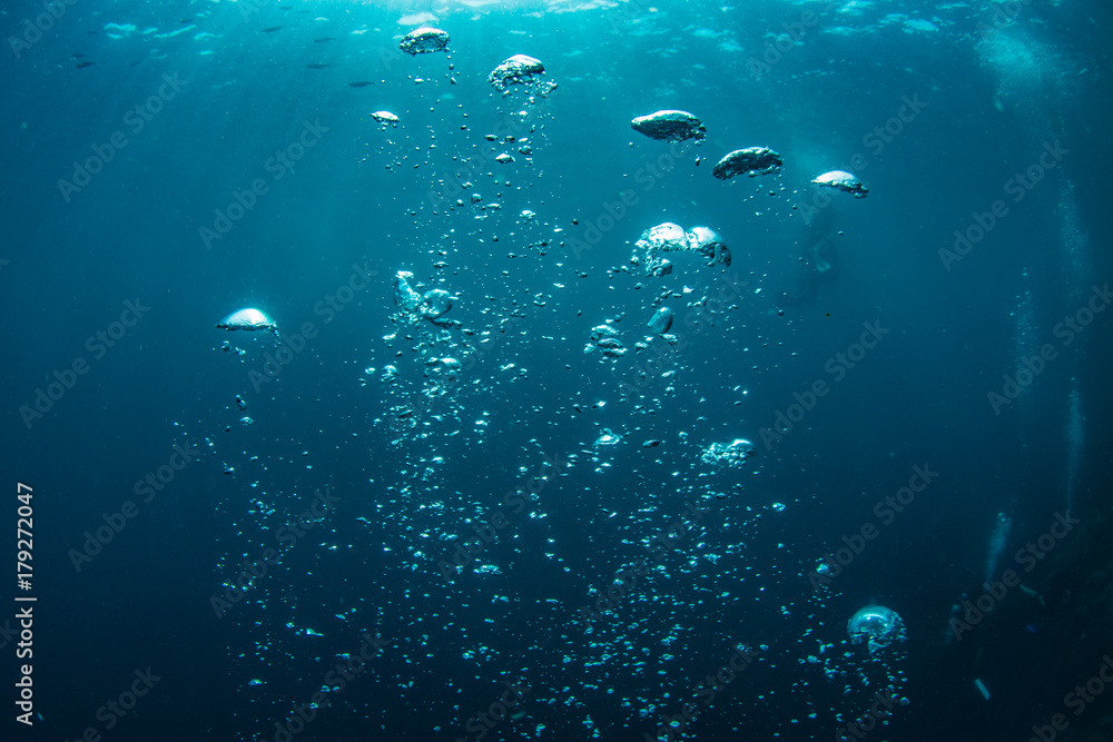 Wall mural underwater shot of blue ocean water, air bubbles closeup, sunbeams on water surface, some scubadiver