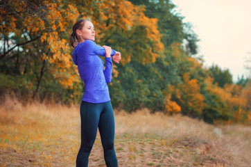 caucasian athletic girl performs warming-up  before jogging on the colorful autumnal forest