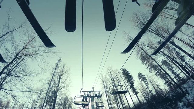 4k footage of 3 skiers going up the hill in the ski lift. Cable lines with empty chairs and trees in the background.