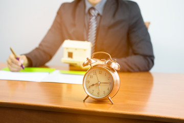 selective focus of alarm clock with Businessman contract signature estate his housing on the desk