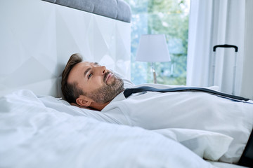 Businessman lying in hotel room bed and relaxing after long day on work trip