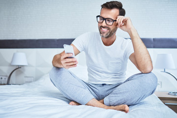 Man sitting on bed and using phone smiling