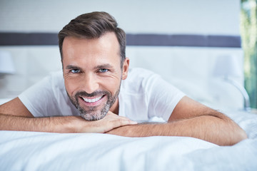 Portrait of smiling man lying on bed and looking at camera