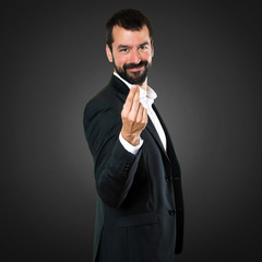 Handsome businessman making money gesture on black background