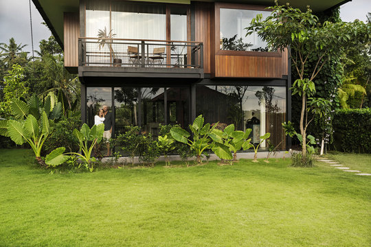 Garden view of couple standing in modern design house surrounded by lush tropical garden