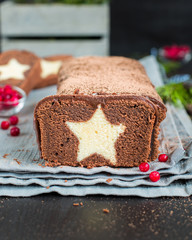 A very chocolate cake covered with dark chocolate and sprinkled with cocoa with a vanilla star inside. On a wooden dark background. Decorated with fresh cranberries, The perfect cool Christmas dessert