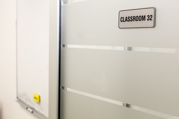 Modern classroom glass doors with number plate; whiteboard in the background.