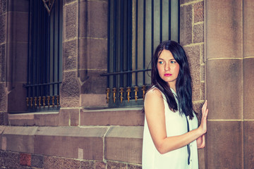 American Woman with long black hair, wearing white sleeveless shirt, standing by vintage wall with...