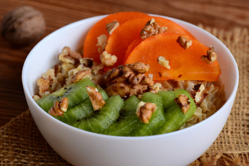 Homemade porridge with toppings. Oatmeal with fresh persimmon, kiwi and walnuts in a bowl and on a wooden background. Healthy porridge for Breakfast. Closeup