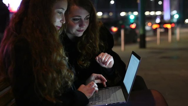 two young women outdoor city night using computer laptop - business, remote woring, technology concept
