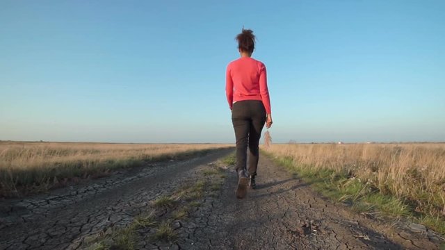 Woman walking along dirt road between fields on sunny day