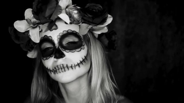 Closeup face of woman with Mexican sugar skull makeup and flowery wreath looking into the camera. Creative, artistic, Halloween concept - black and white video