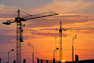 Building crane against the beautiful sunset sky. Silhouettes of building cranes at sunset. Construction crane at sunset.