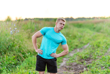 Fototapeta premium Bodybuilder gymnastics in the park in a T-shirt. Summer lifestyle is outdoor recreation, motivation is strong. Muscular arms.