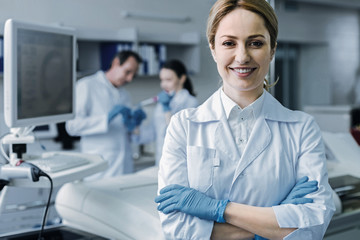 Fototapeta premium Professional science. Confident nice female scientist standing cross handed and smiling while looking at you