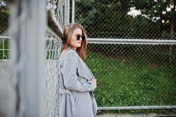 Girl in gray coat with sunglasses at small street stadium.