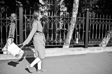 Girl in gray coat with sunglasses and handbag walking at street against iron fence.