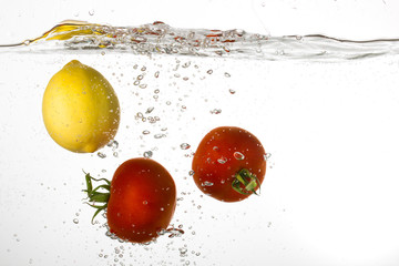 Two red tomateos and yellow lemon falling into water