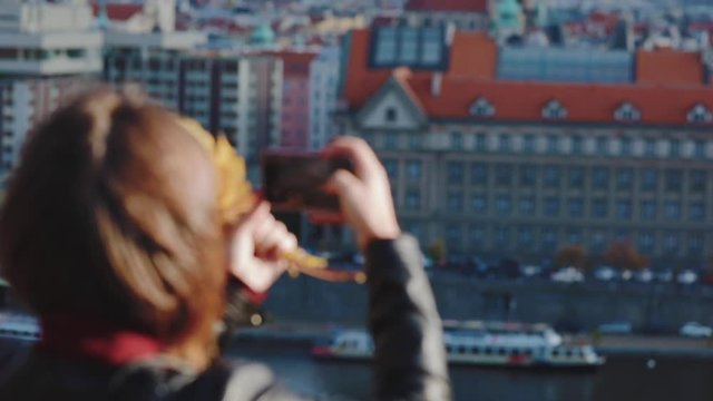 The girl photographs a city landscape - beautiful roofs of houses in Prague. The tourist shoots with phone city sights in Prague. Video in slow motion