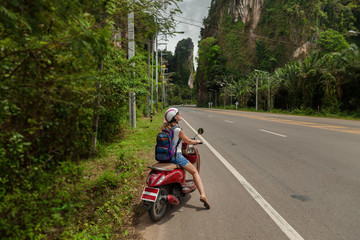 tourist woman sitting on classic scooter against the background of the mountains of Krabi Province,...